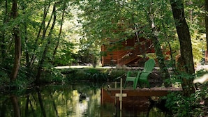 A wooden cabin with a dock and a green chair by a calm pond surrounded by dense trees. - Olivers Hideaway | on Fightingtown Creek (Cherry Log)