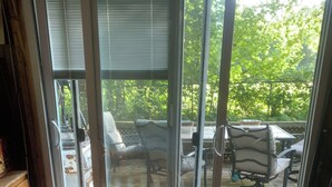 Habitació amb llit, sòl de fusta i porta corredissa de vidre que dona a un patí exterior amb cadires i taula.