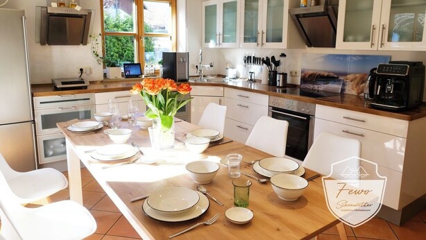 Una cocina moderna con armarios blancos, una isla de madera y un comedor preparado para seis comensales.