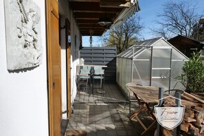 A patio with a wooden table and chairs, a greenhouse, and a carved stone relief. - FeWo Schönwetter - Center (Weßling)