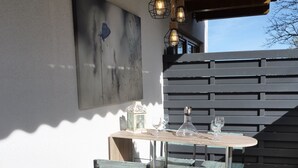 Un patio al aire libre con una mesa y sillas de madera, una lámpara colgante y un cuadro sujeto a la pared.