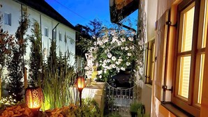 Un sendero estrecho que lleva a un edificio blanco con jardín, una lámpara decorativa y una reja.