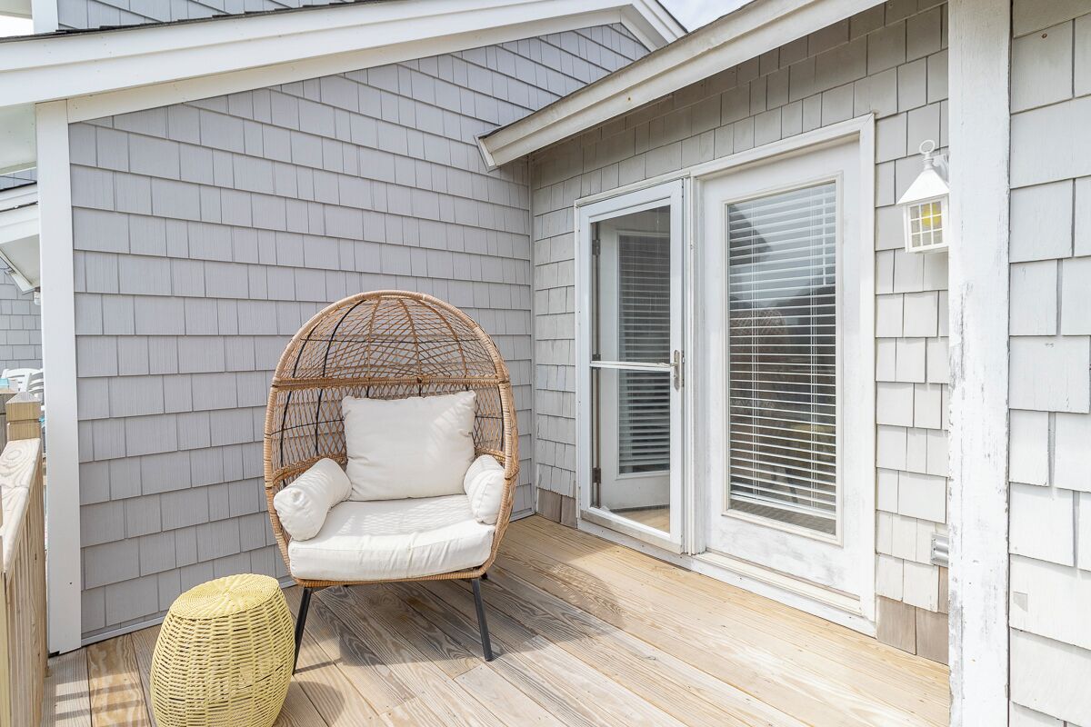A covered porch with a wicker chair and ottoman, a sliding glass door, and a white lantern.