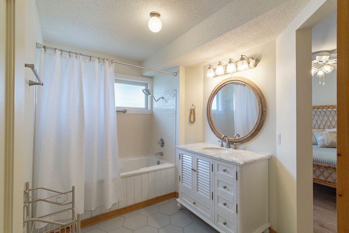 A bathroom with a bathtub, a vanity with a mirror, and a shower curtain.