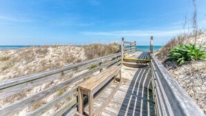 Une promenade en bois qui mène à une plage, avec un ciel bleu dégagé.