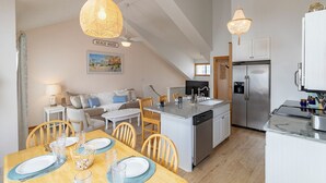 Une cuisine compacte dotée d’un îlot central, un coin repas avec une table pour quatre personnes et un espace salon avec un canapé et des fauteuils.