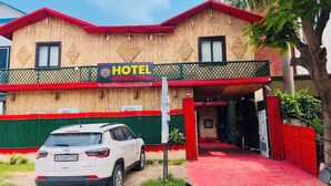 Um hotel com fachada de bambu, telhado vermelho e uma placa indicando ser o "HOTEL ARCADIA PLUS".