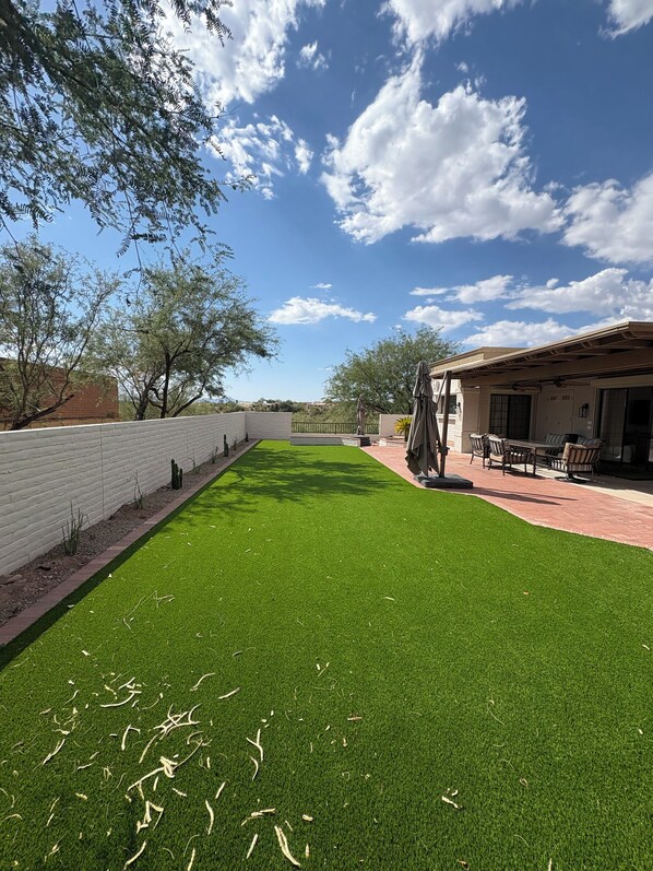 A patio area with artificial grass, outdoor furniture, and a building with a brick facade.