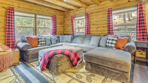 A cozy cabin interior with a sectional sofa, ottoman, and a wooden ceiling. - Cabin ~ 1 Mi to Lake Gregory & Hiking! (Crestline)