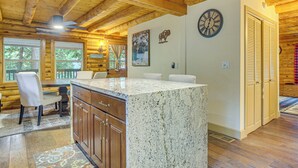 A wooden interior with a kitchen island, dining area, and a clock on the wall. - Cabin ~ 1 Mi to Lake Gregory & Hiking! (Crestline)