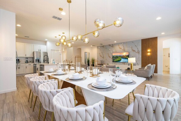 A modern dining area with a white table set for six, surrounded by tufted chairs with gold legs. - Stunning Home 9 Ensuites Near Disney (2615SN) (Kissimmee)