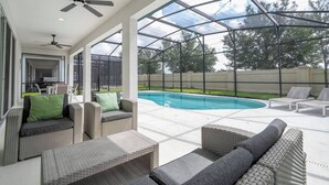 Ein überdachter Außenbereich mit Pool, Korbmöbeln, Deckenventilatoren und einer Glaskonstruktion.