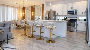 Una cocina moderna con armarios blancos, electrodomésticos de acero inoxidable y una isla central con taburetes de bar.