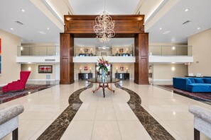 A spacious lobby with a central round table, a chandelier, and a blue sofa.