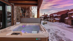 A hot tub with a control panel, surrounded by stone walls and wooden beams, with snow-covered roofs in the background. - Tristant 125- Luxury Ski-In/Out Chalet with Hot Tub (Mountain Village)