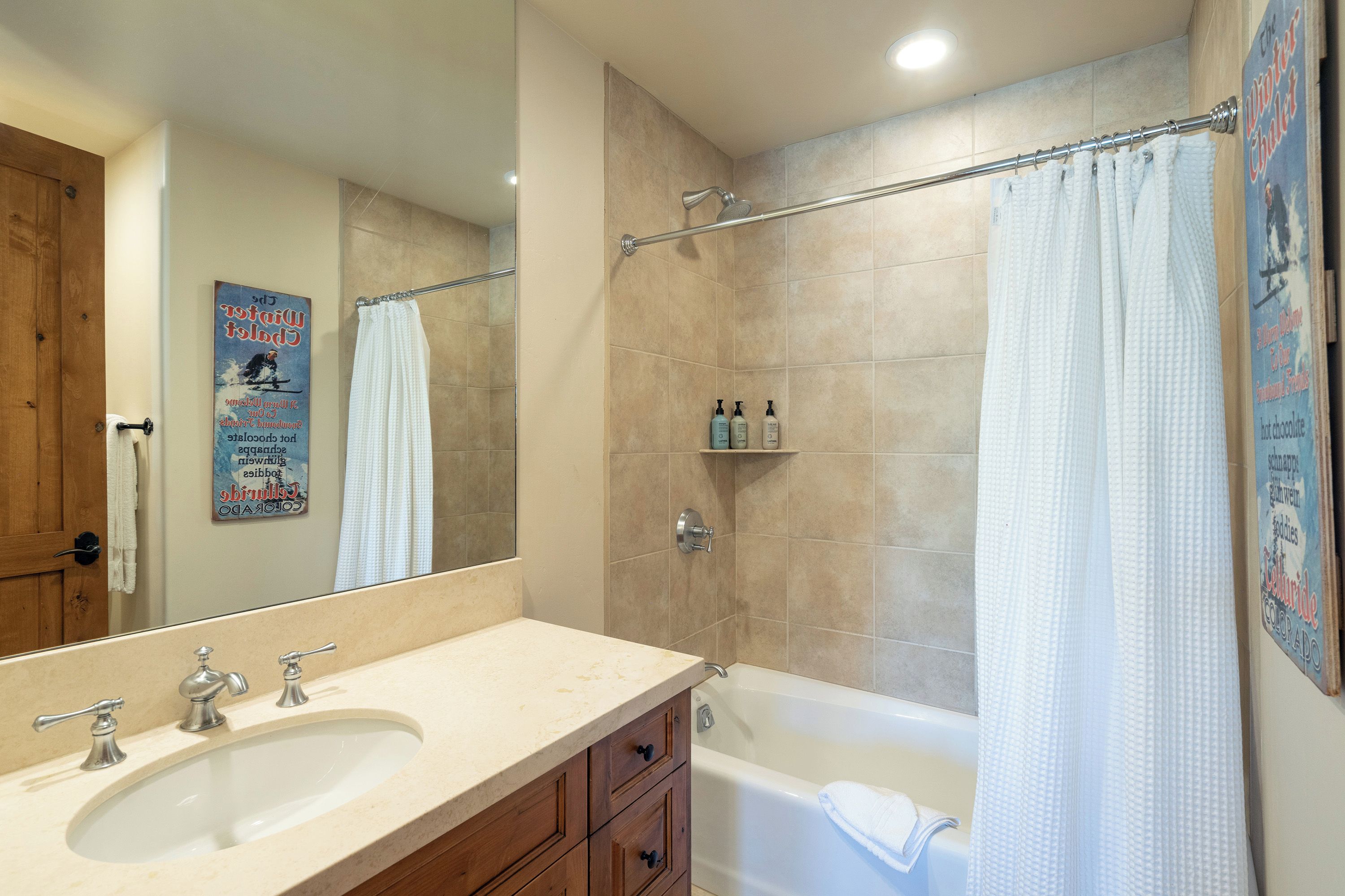 A bathroom with a bathtub, a shower, a sink, and a mirror. There are toiletries on the wall and a towel rack.