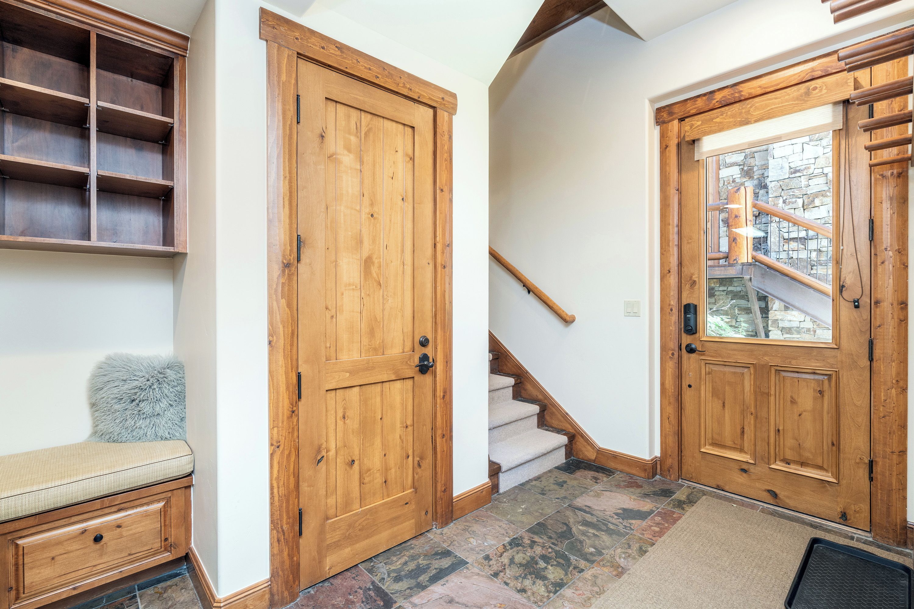 A hallway with wooden doors, a staircase, and a bench.