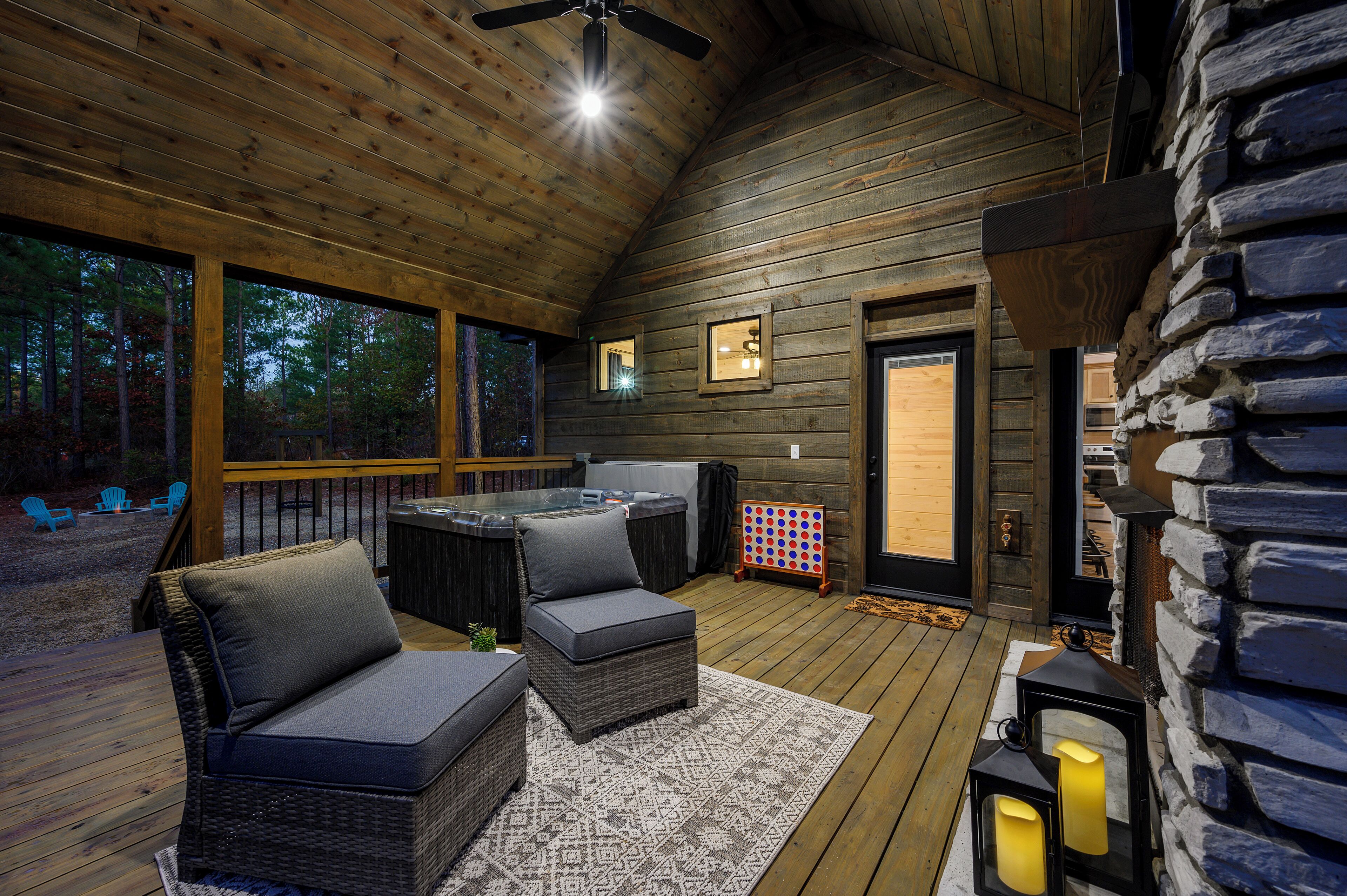 A wooden deck with wicker furniture, a hot tub, and a stone fireplace.