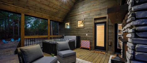 A wooden deck with wicker furniture, a hot tub, and a stone fireplace.