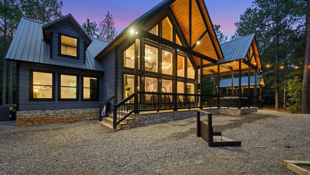 A modern log cabin with large windows, a stone foundation, and a gravel driveway. - NEW Listing Discounts! LUX+Amenities for everyone! (Broken Bow)
