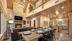 A spacious living area with a fireplace, a dining table set for six, and a kitchen in the background. - NEW Listing Discounts! LUX+Amenities for everyone! (Broken Bow)