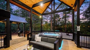 A covered outdoor deck with a hot tub, wooden furniture, and string lights. - NEW Listing Discounts! LUX+Amenities for everyone! (Broken Bow)
