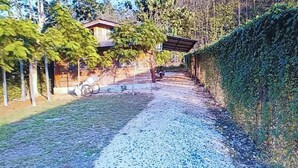 Un chemin de gravier mène à un bâtiment doté d’un porche abrité, entouré d’arbres et d’une haie.