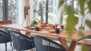A breakfast table with croissants, fruits, and beverages, set in a bright room with large windows.