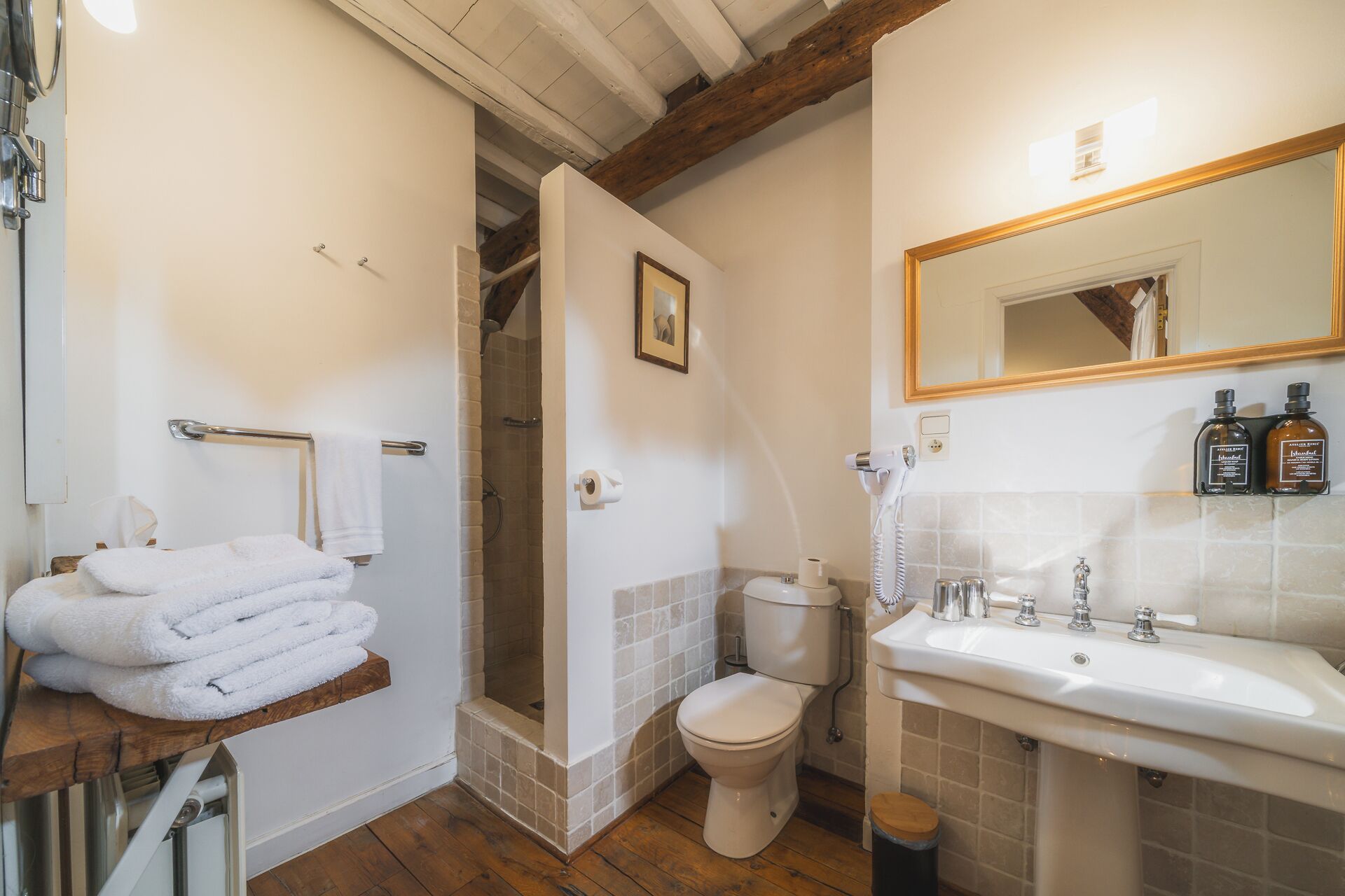 A bathroom with a shower, toilet, and sink, featuring a wooden beam ceiling and tiled walls.