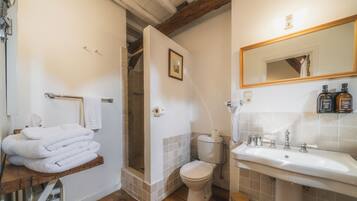 A bathroom with a shower, toilet, and sink, featuring a wooden beam ceiling and tiled walls.