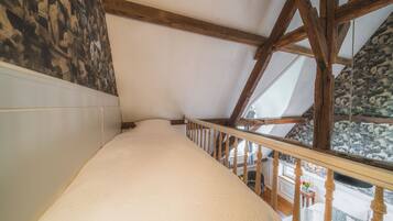 Une pièce avec un plafond en pente, des poutres en bois, un lit blanc et une vue sur un mur de pierre orné d’œuvres d’art.