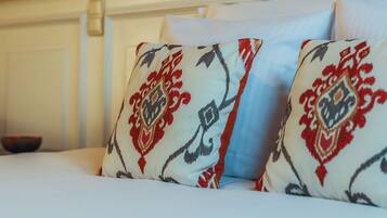 A bed with white bedding and patterned pillows, a wall-mounted lamp, and a white headboard.