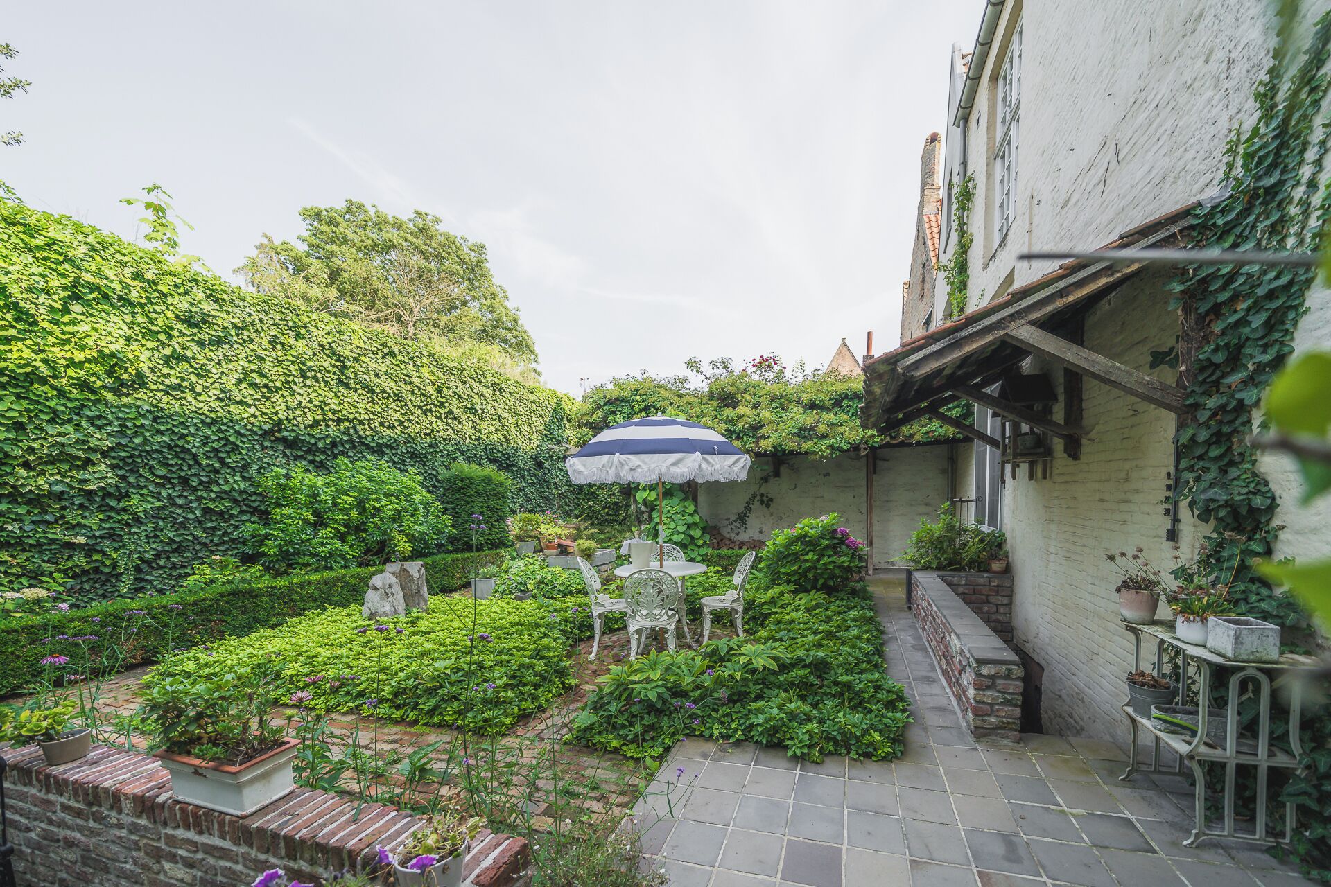 Un jardin agrémenté d’un espace patio comprenant une table et des chaises, le tout entouré d’une végétation luxuriante et de plantes en pot.