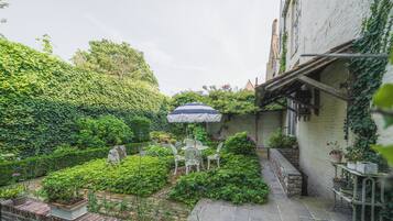 Un jardin agrémenté d’un espace patio comprenant une table et des chaises, le tout entouré d’une végétation luxuriante et de plantes en pot.