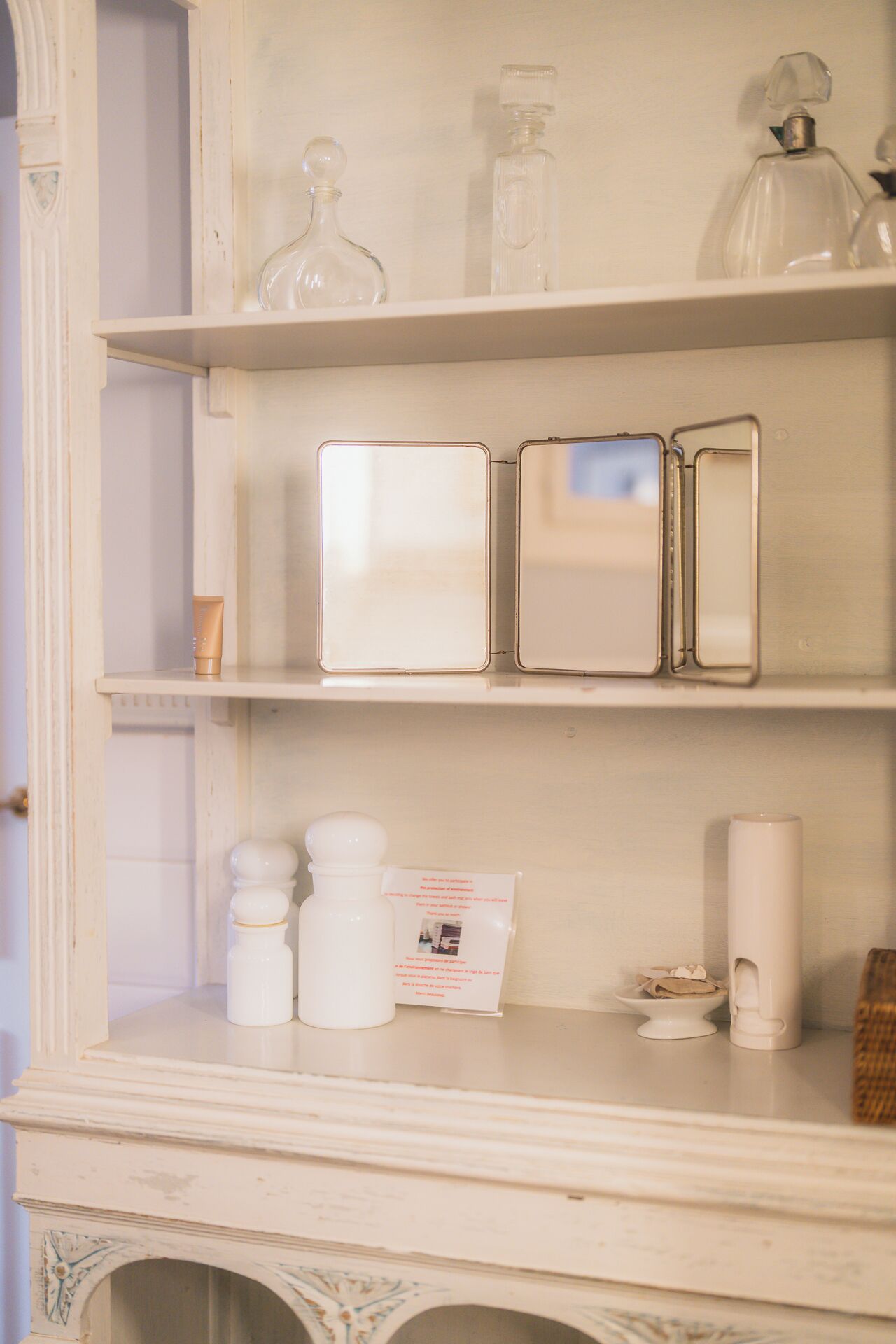 Une salle de bain avec un meuble-lavabo blanc, un meuble à miroir et une étagère contenant des articles de toilette.