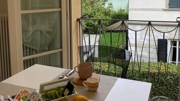 Un balcon avec une table préparée pour le petit-déjeuner, une vue sur un bâtiment surmonté d’un dôme et un jardin.