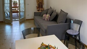 Un salon avec un canapé gris, une table à manger agrémentée d’un centre de table floral et une table basse en verre.
