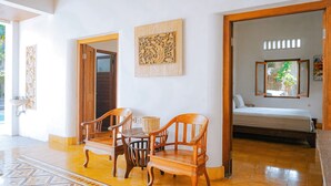 Ein Zimmer mit einem Bett, Holzsesseln, einem Tisch und einem an der Wand befestigten Kunstwerk.