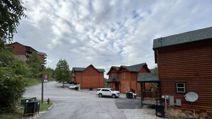 Un bâtiment de style cabane en rondins, avec une allée pavée et un VUS blanc garé devant.