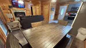 Un intérieur en bois comprenant une grande table à manger, un canapé, un téléviseur et un coin cuisine.