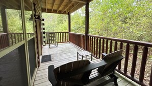 Une terrasse extérieure couverte, dotée d’une table et de chaises en bois, entourée d’une balustrade en bois et offrant une vue sur une zone boisée.