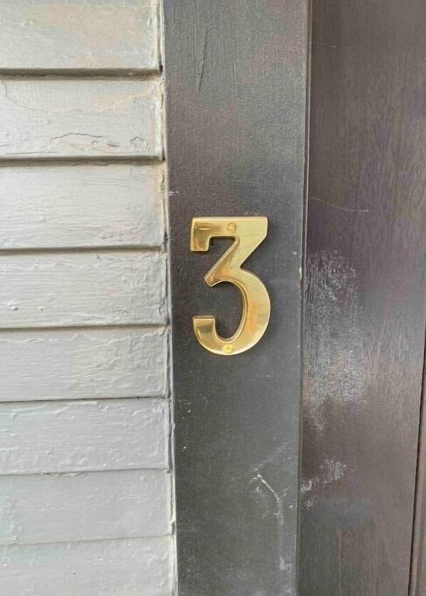Un numéro de maison en laiton, le chiffre « 3 », fixé sur une porte sombre.