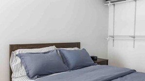 Une chambre à coucher avec un lit, des oreillers, une table de chevet et un téléviseur fixé au mur.