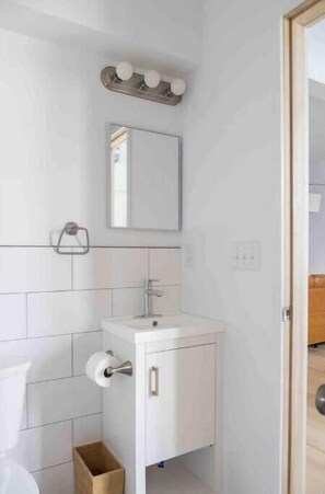 A modern bathroom with white tiles, a sink, a mirror, and a vanity with a towel rack. - Urban Luxury Loft: Parking+72”TV (Burlington)