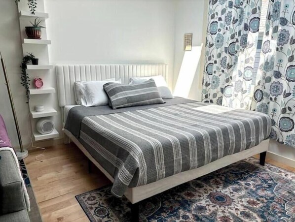 A neatly arranged bedroom with a bed, bedside tables, a radiator, and a patterned rug. - Urban Luxury Loft: Parking+72”TV (Burlington)