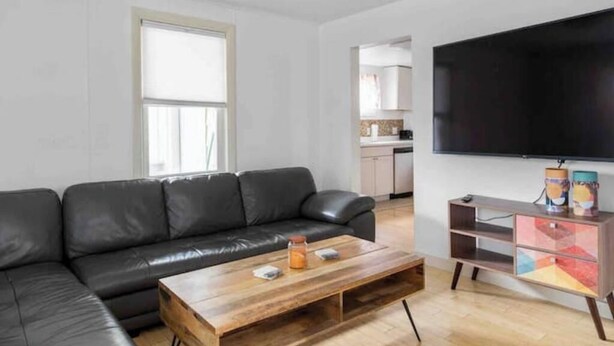 Una sala de estar moderna con un sofá de cuero negro, una mesa de centro de madera y un aparador colorido.