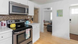 Una cocina moderna con armarios blancos, un microondas de acero inoxidable, un hervidor amarillo y un salpicadero de azulejos.