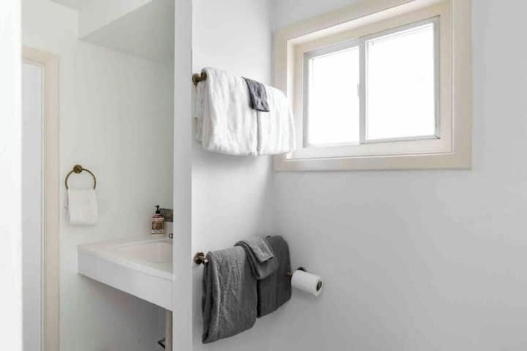 Un bagno con un lavandino bianco, una finestra e asciugamani appesi a un porta asciugamani.