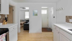 Una cocina moderna con armarios blancos, suelo de madera y vistas al salón.