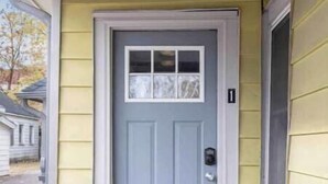 Una casa de un solo piso con una puerta delantera gris, un ventanal pequeño sobre la puerta y un letrero con el número '1'.